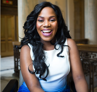 A brown skinned woman with long flowing hair smiling with excitement.