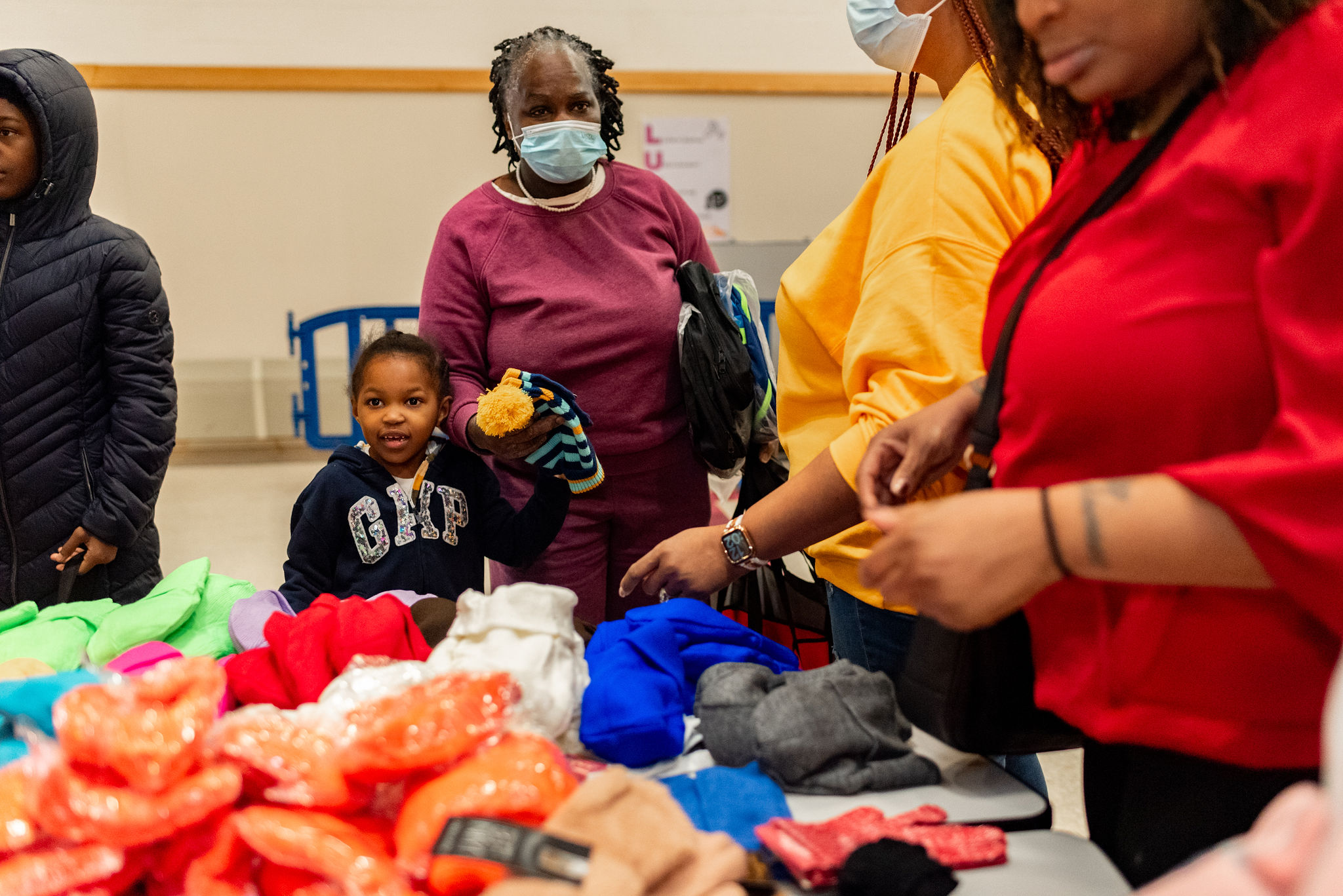 A child holding an adults hand as they direct their gaze toward clothing apparel on a table . 